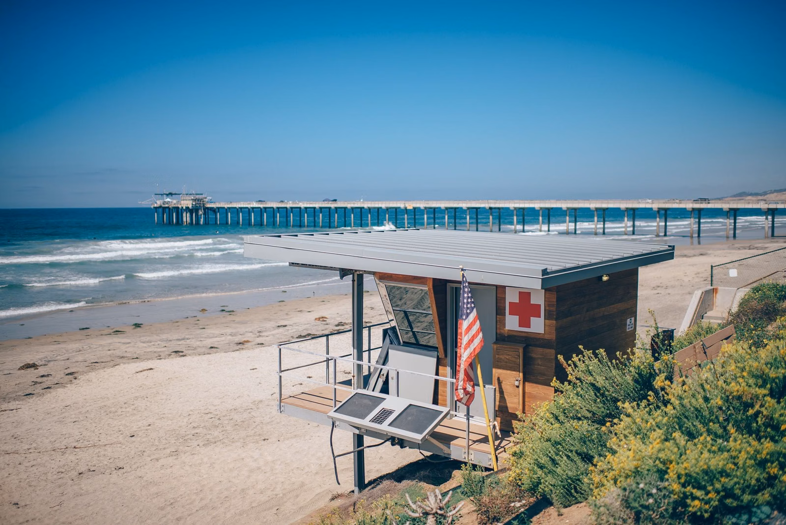 A lifeguard tower on a Southern California beach with a pier in the distance