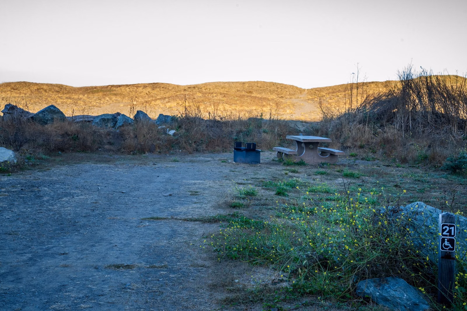 A paved campsite with a picnic table and fire ring, marked with an accessible-site post