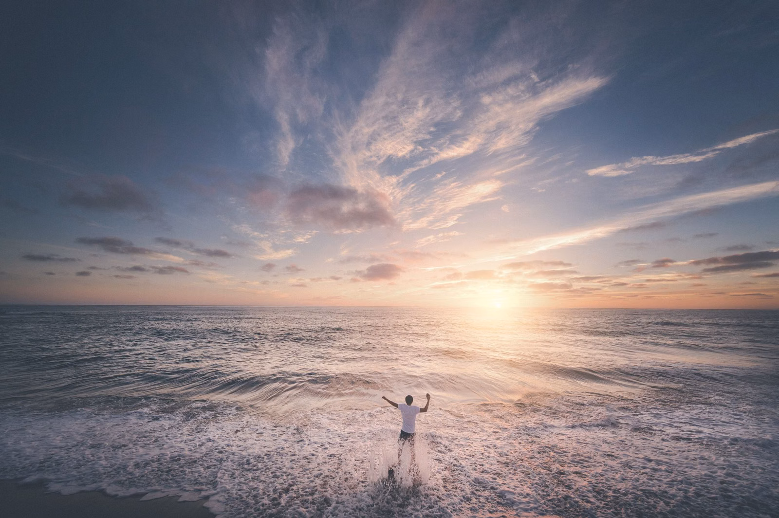 A person standing at the water's edge at sunset on a Southern California beach